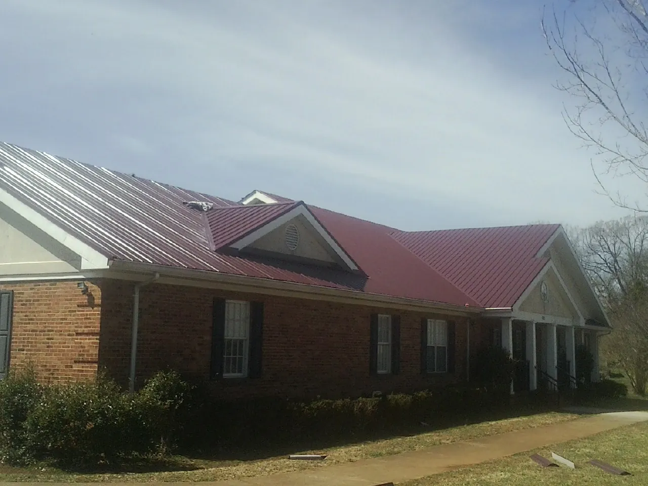 Red metal roof with gabled entries on a long brick building, from a Hail Damage Roof Repair job in Coudersport
