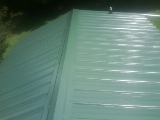 New green metal panels meeting at the ridge of a roof — Flat Roof Repair work by our crew in Coudersport