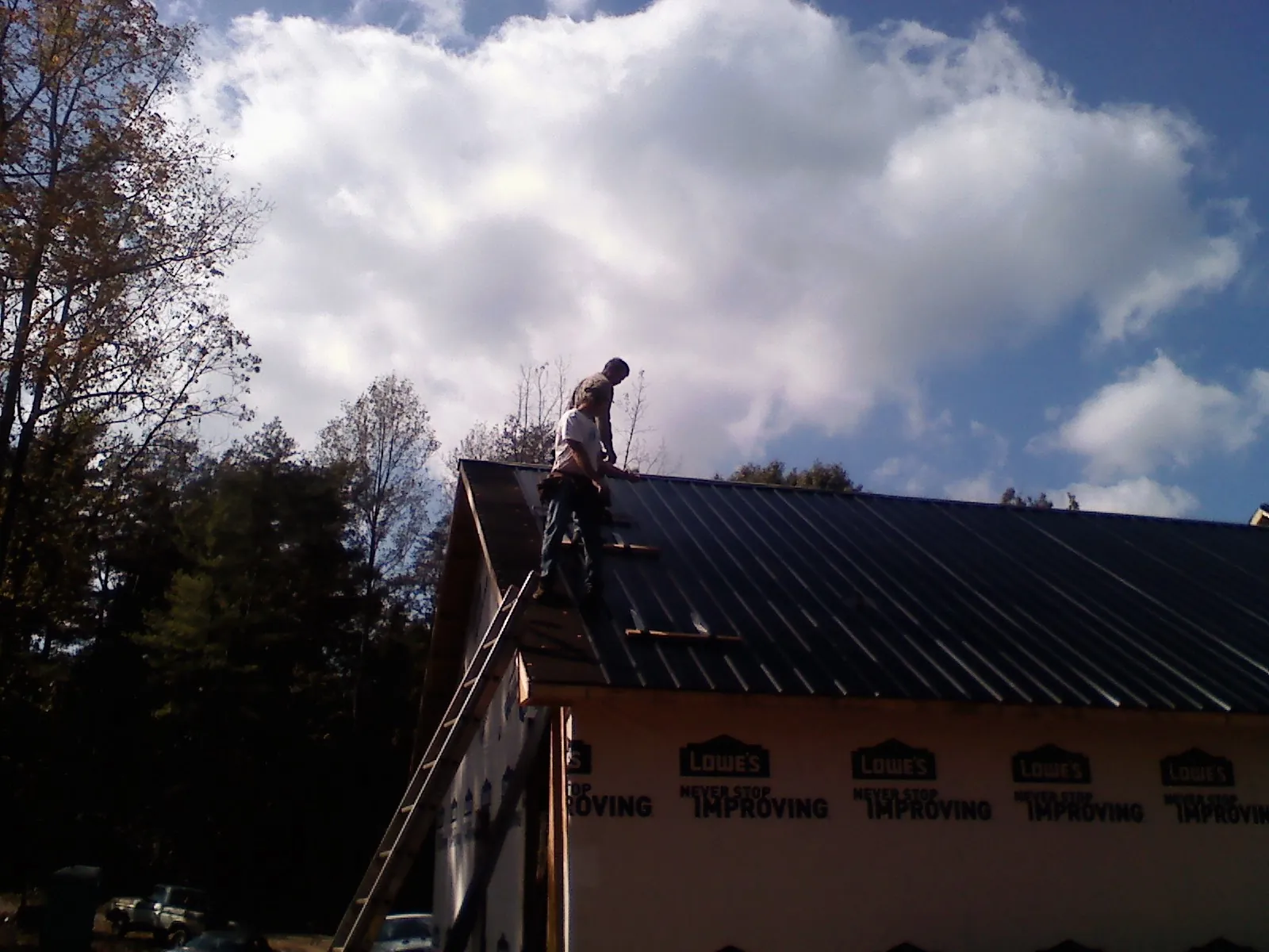 Roofer fastening dark metal panels high against a cloudy sky, from a Roof Inspection job in Coudersport