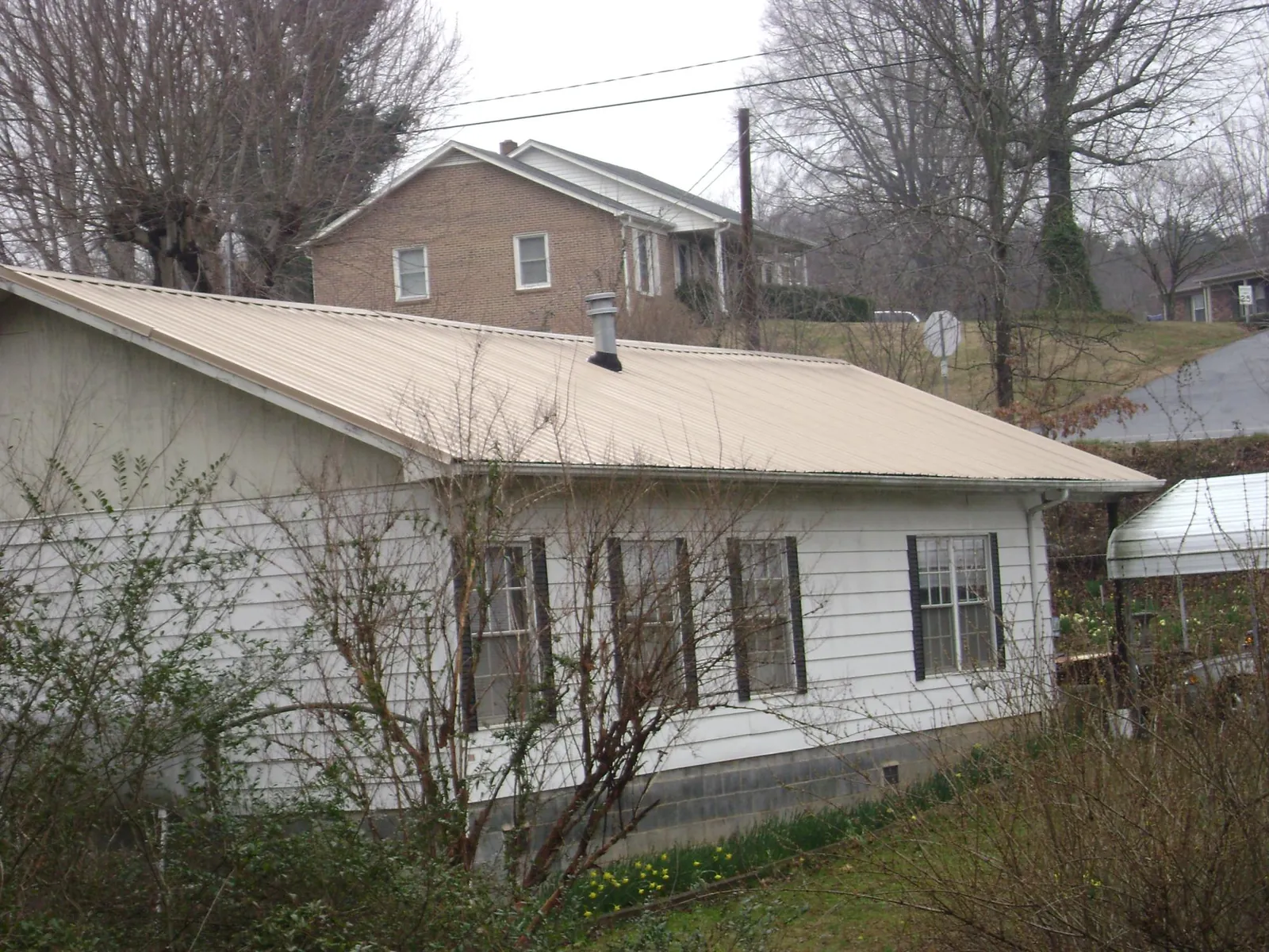 Tan metal roof on a white sided house set into a hillside — Commercial Roofing by Roofing Brothers in Coudersport