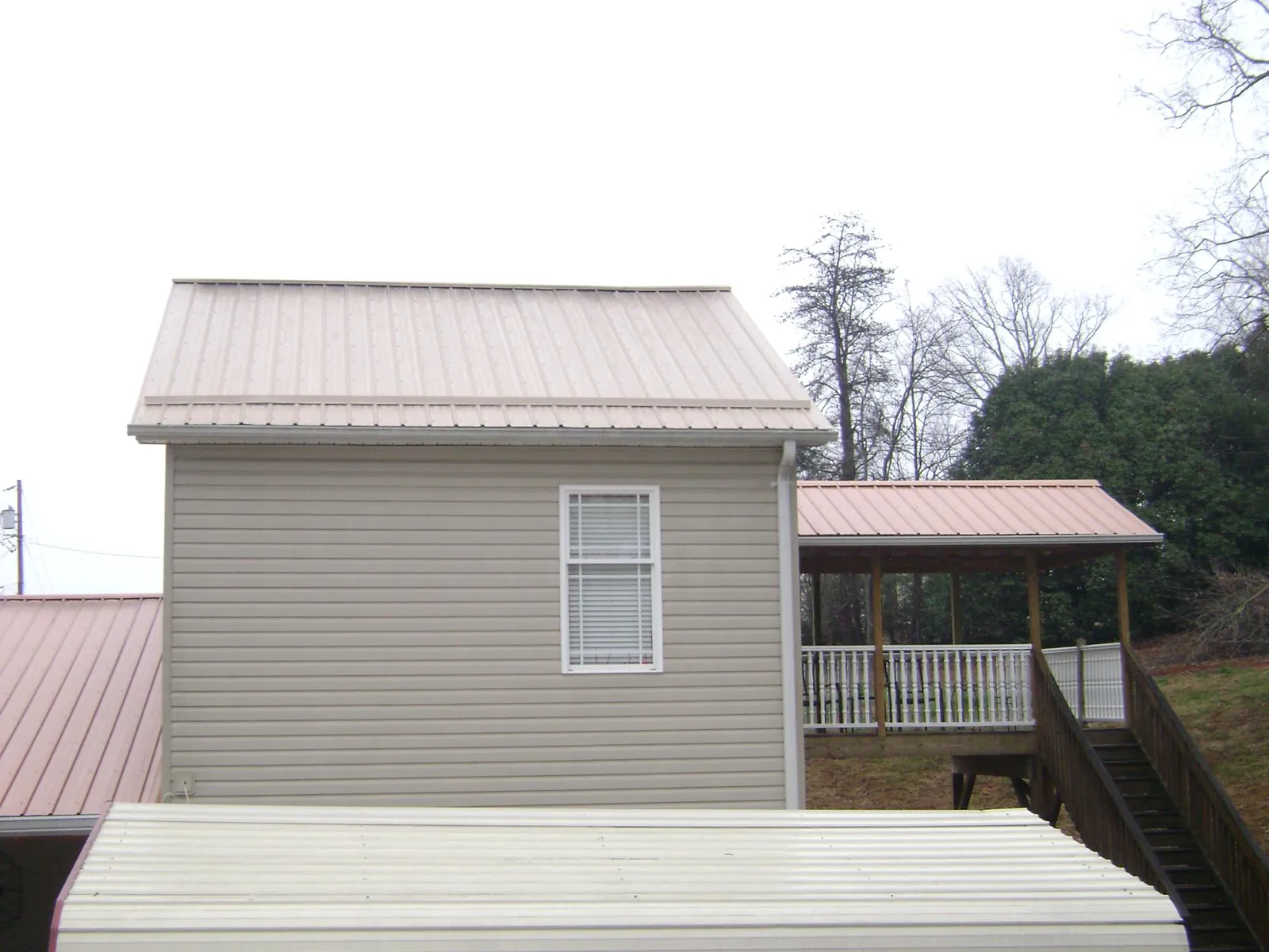 Tan metal roofs on a two story addition and attached porch, from a Roof Replacement job in Coudersport