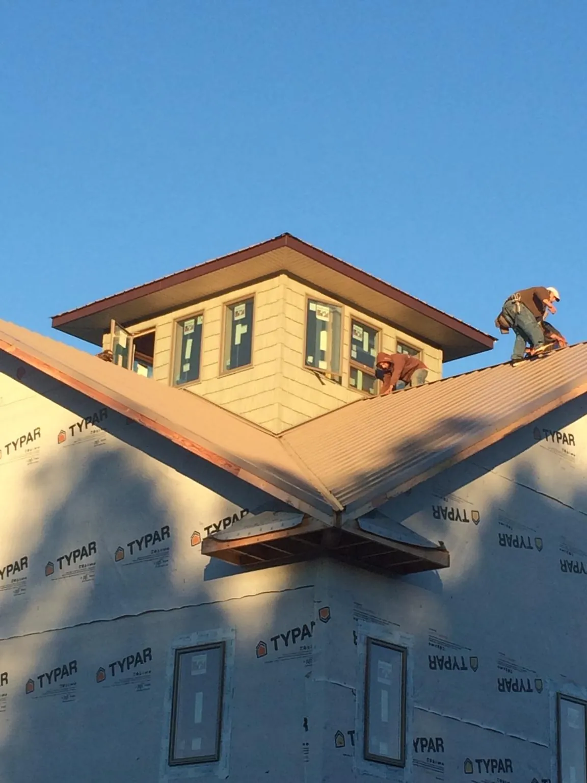 Roofers working around a rooftop cupola on a new metal roof at sunset — Roof Waterproofing in Coudersport by Roofing Brothers